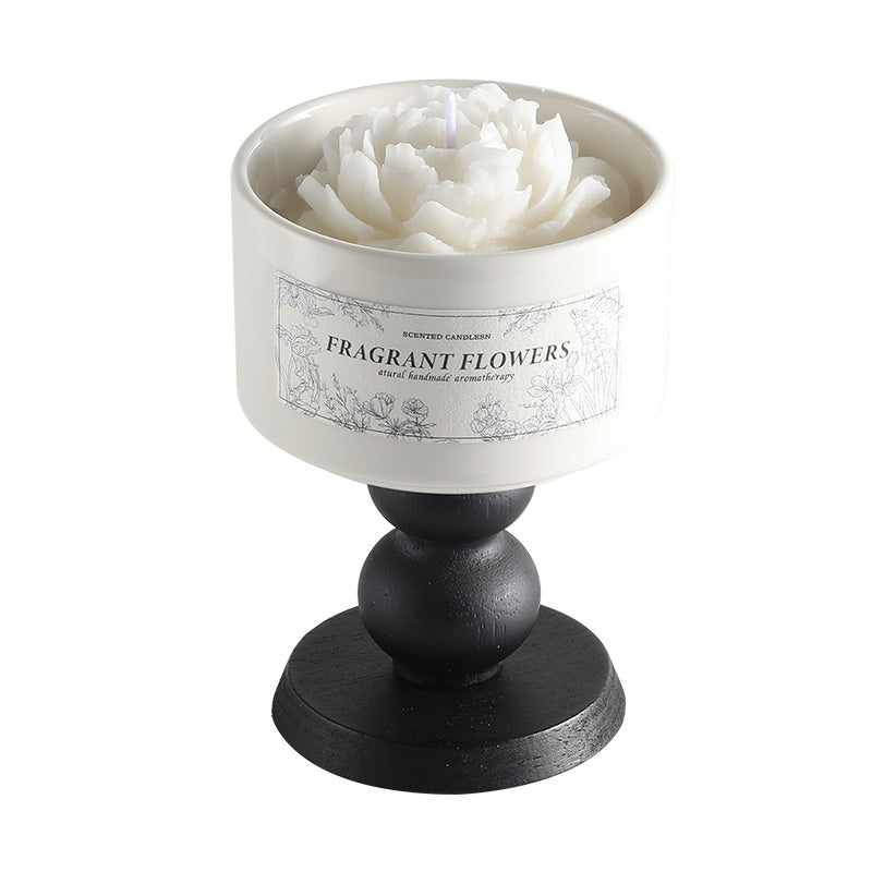 A minimalist white Camellia Scented Candle on a vintage black wooden pedestal base featuring a white blooming flower design.