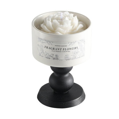 A minimalist white Camellia Scented Candle on a vintage black wooden pedestal base featuring a white blooming flower design.