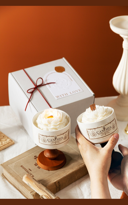 A person holding a white Camellia porcelain cup candle next to its elegant white gift box with a "With Love" tag and red ribbon.