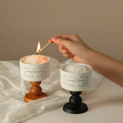 A hand lighting the flower-shaped white camellia scented soy candle on a wooden pedestal with a match.