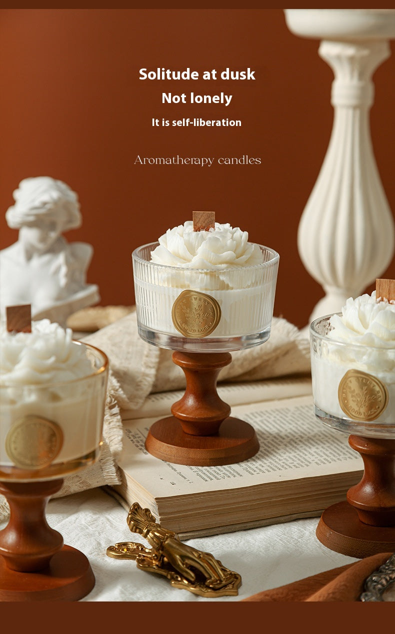 Three white camellia-shaped aromatherapy candles in ribbed glass cups with wooden pedestals, featuring wooden wicks and botanical essential oils.