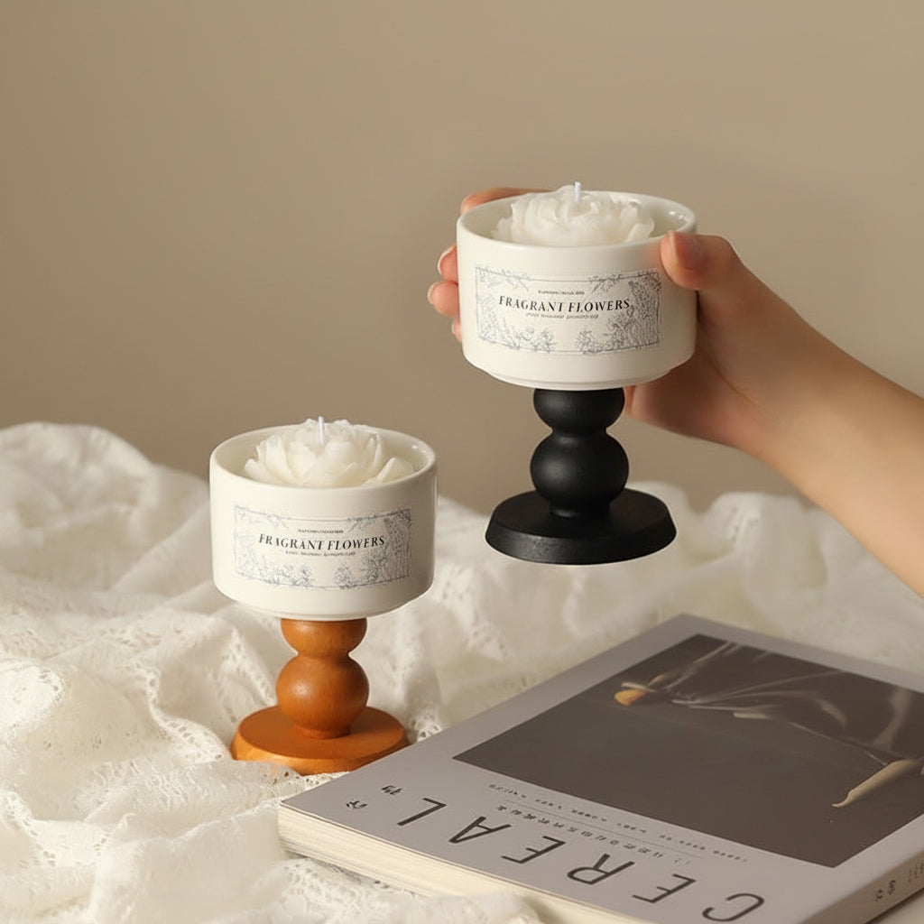 Close up of hands holding a lit white flower-shaped relaxation candle in front of a Delphy luxury white gift box.