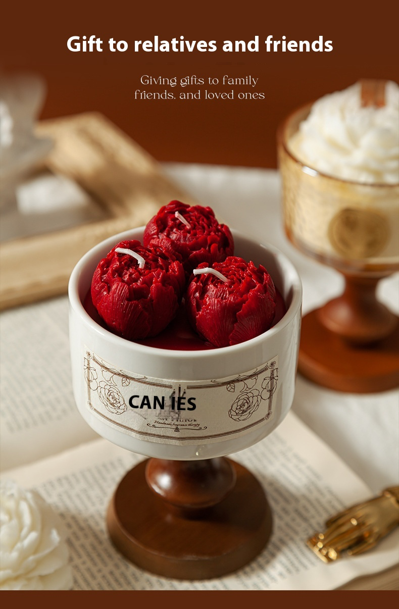 A white porcelain cup candle featuring three vibrant red peony-shaped wax carvings, resting on a wooden base with a vintage aesthetic.