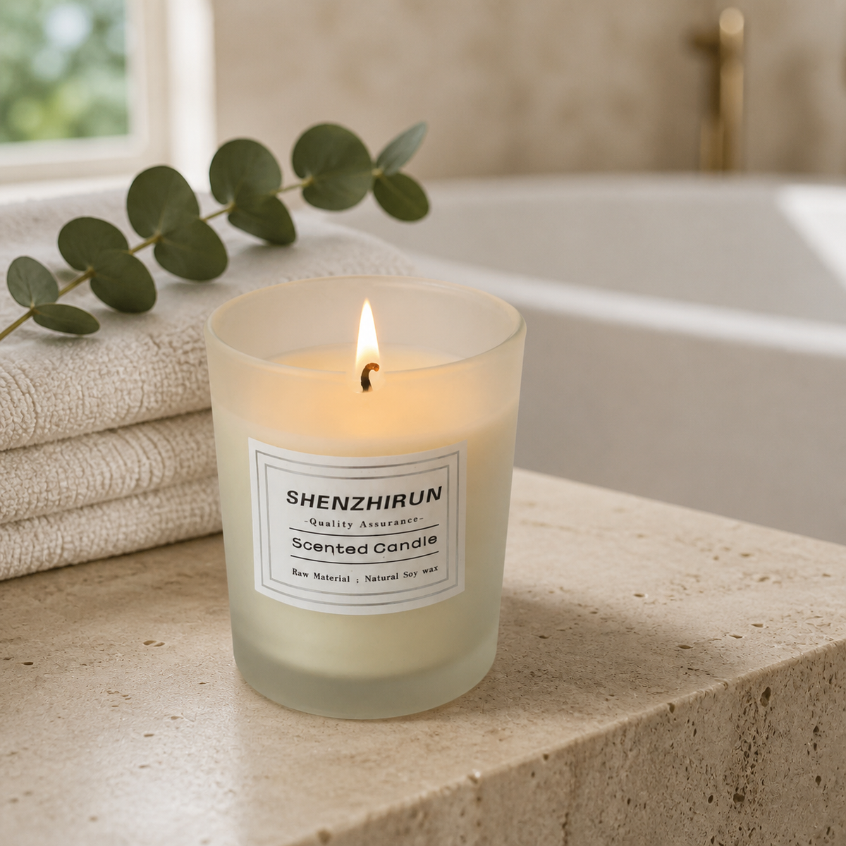 Lit Stress Relief Soy Candle in white frosted glass on a travertine bathroom ledge with towels and eucalyptus.